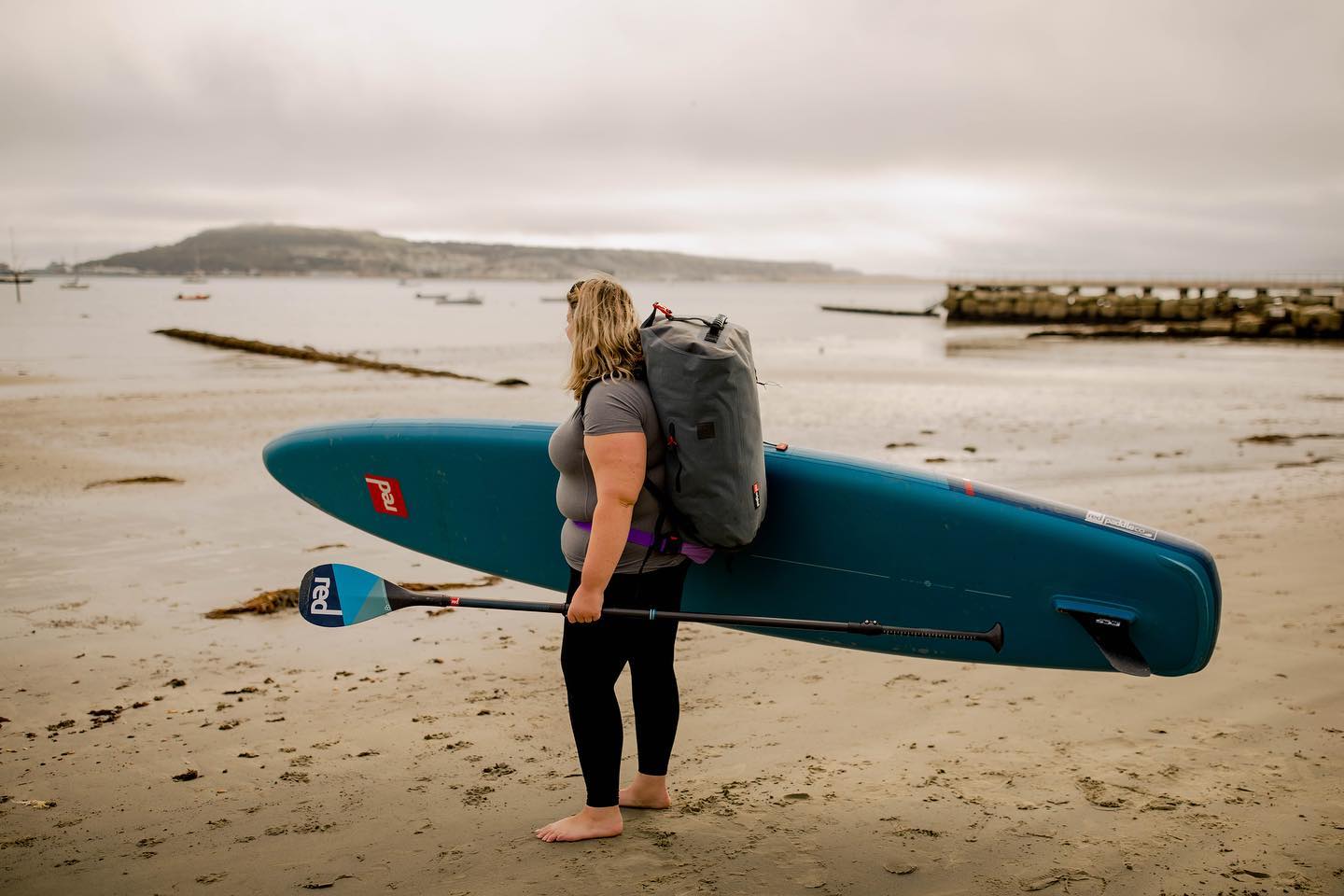 woman carrying red touring paddle board on the beach
