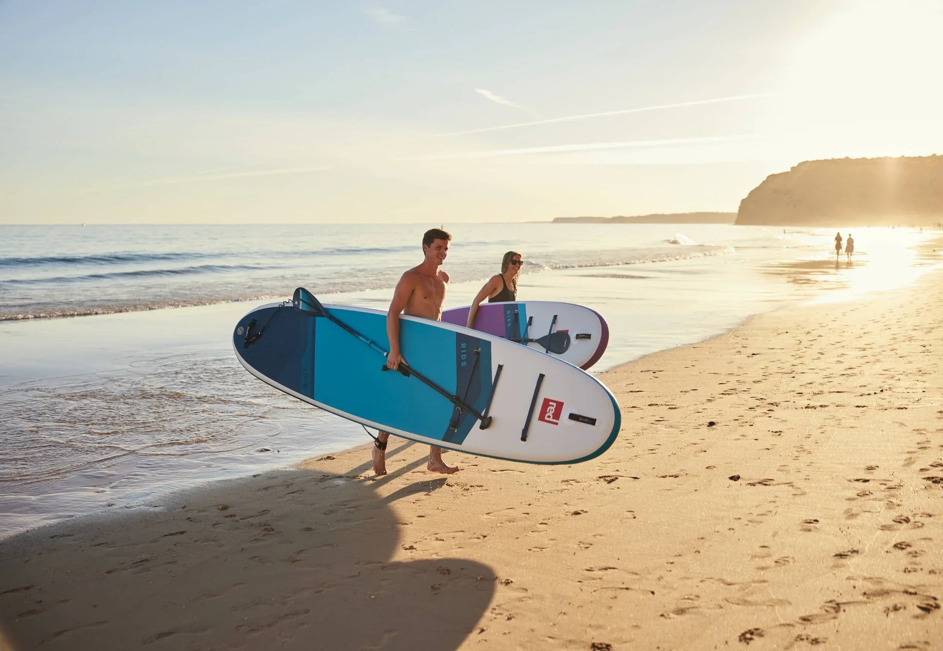 man and woman exiting water holding red paddle co inflatable paddle boards