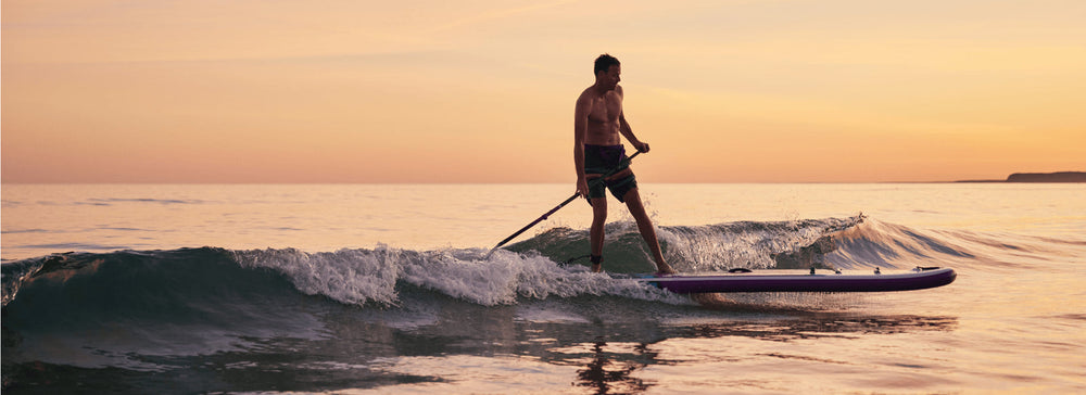 A man stand up paddleboarding in the sea at sunset