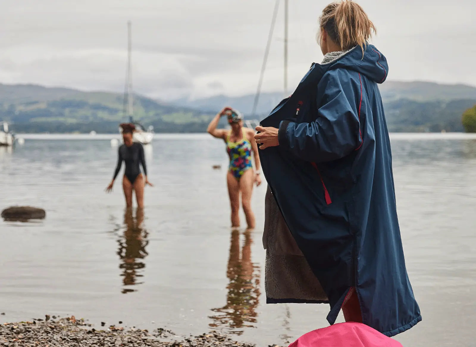 A woman wearing her pro change robe and 2 other woman paddling in the sea