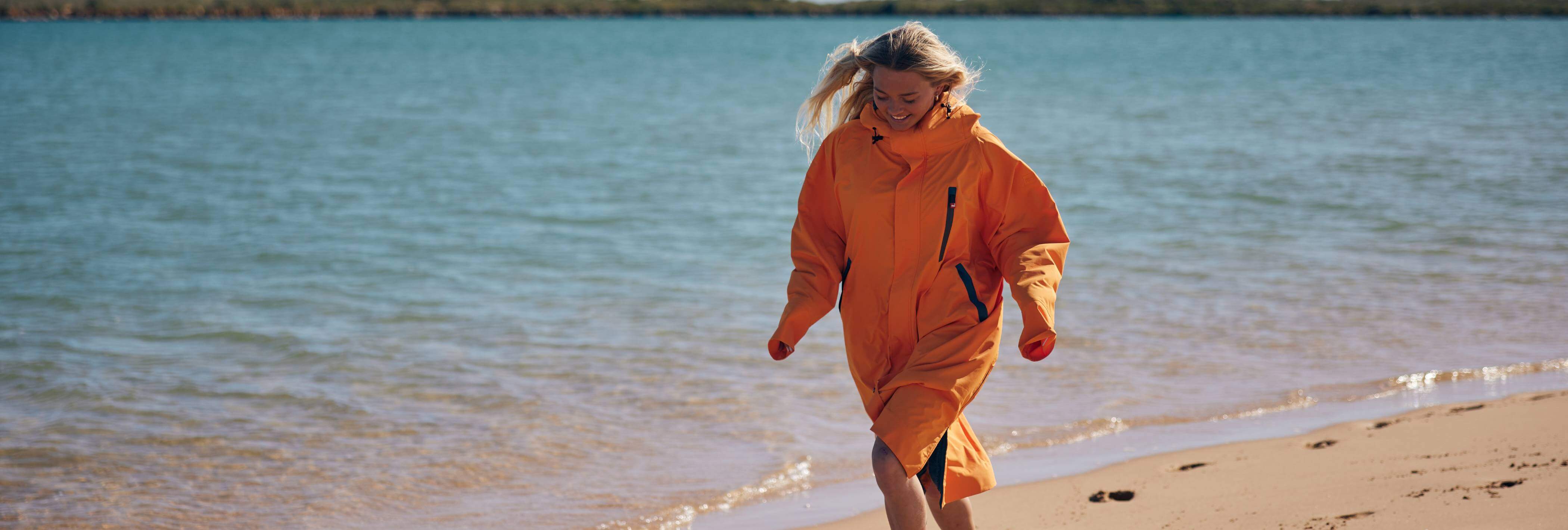 woman walking on sand wearing orange changing robe