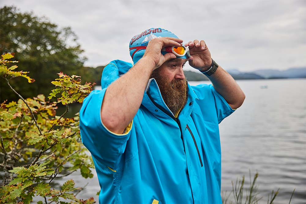 Man stood by the sea wearing Red Original changing robe and swimming goggles