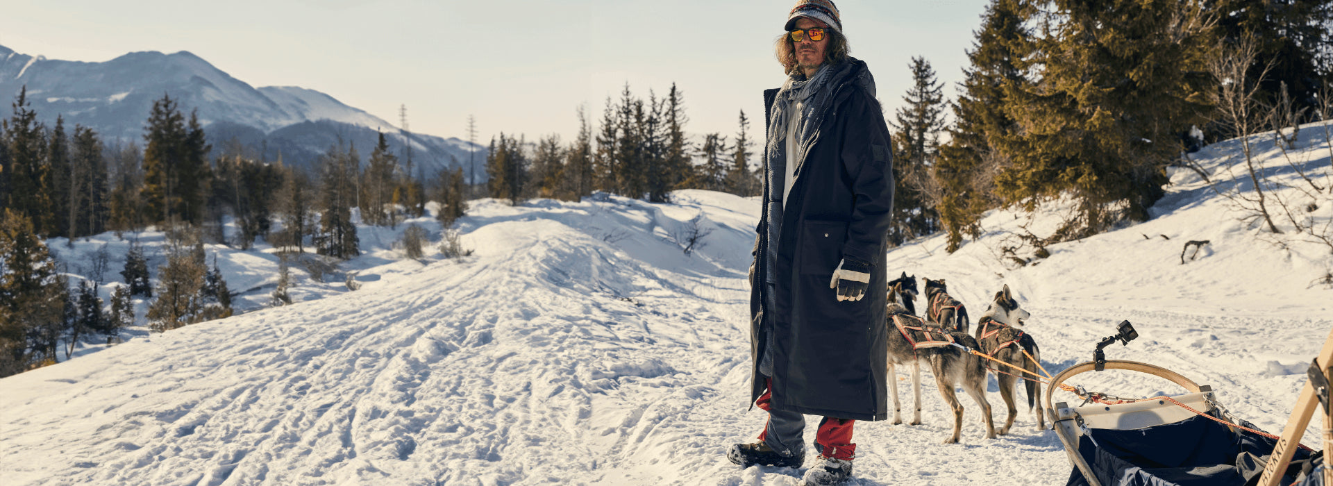 A man hiking in the snow while his dogs are pulling a sled