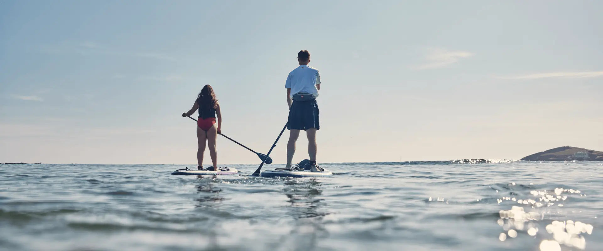 two paddleboarders paddling towards horizon