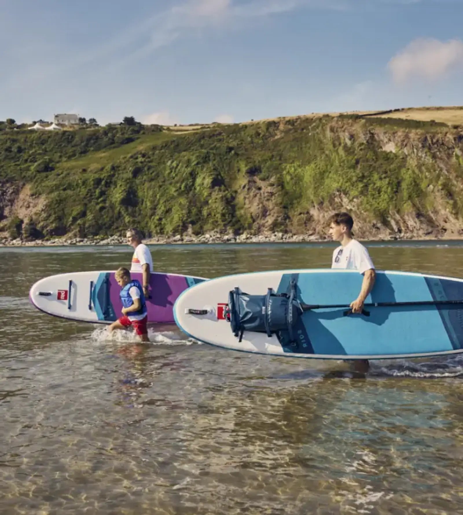 A family carrying their paddleboards into the sea on a sunny day