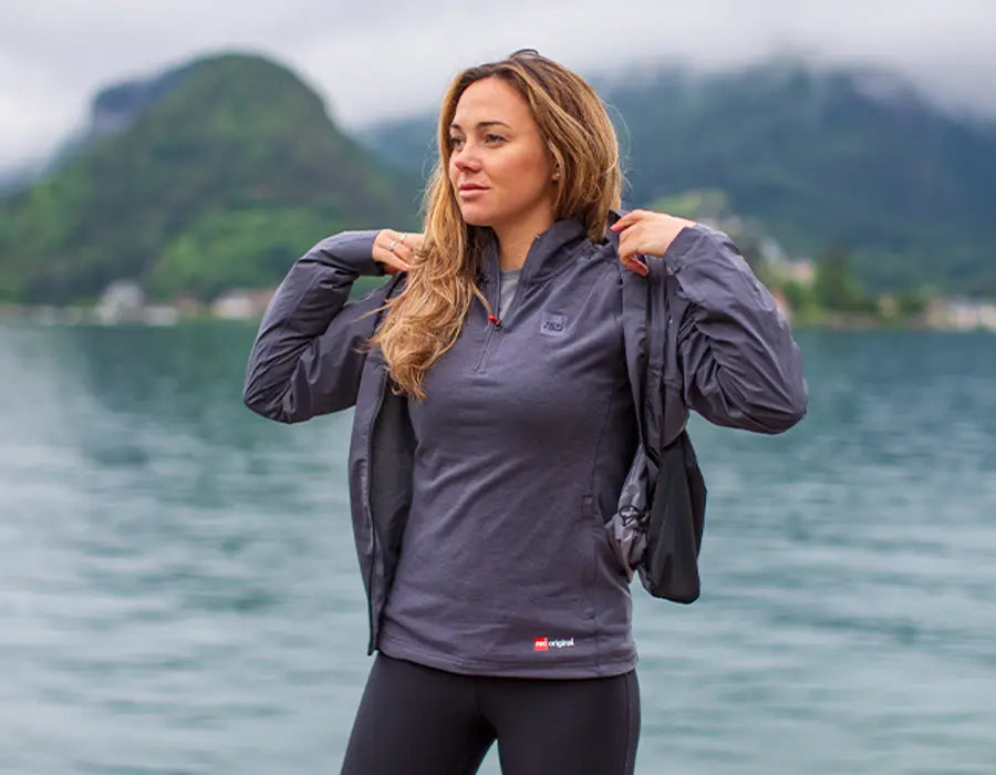 A woman putting on her Red Active Jacket by the ocean