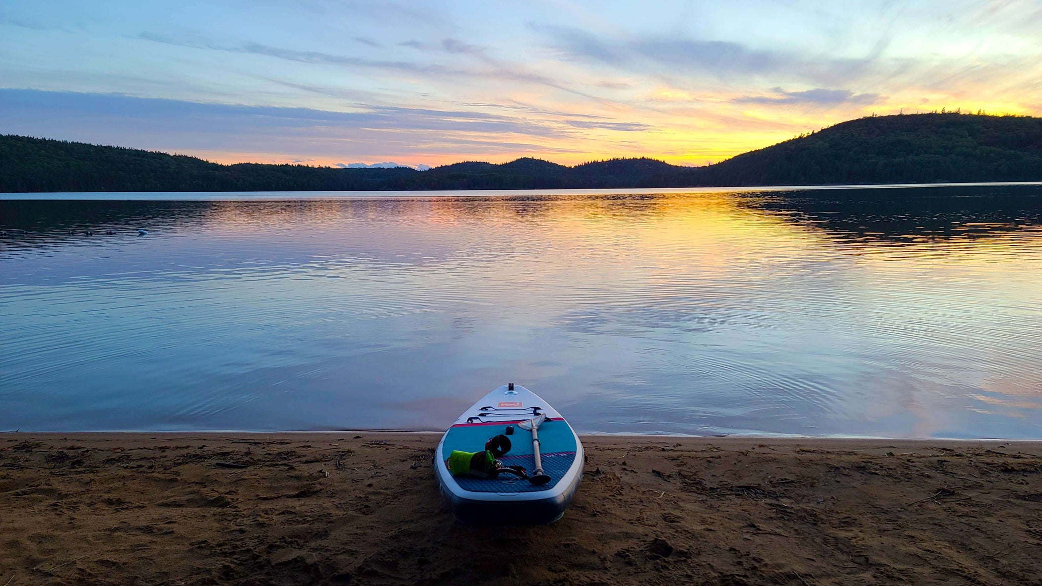 picturesque view of a lake at sunset with a Red inflatable paddle board placed on the shoreline