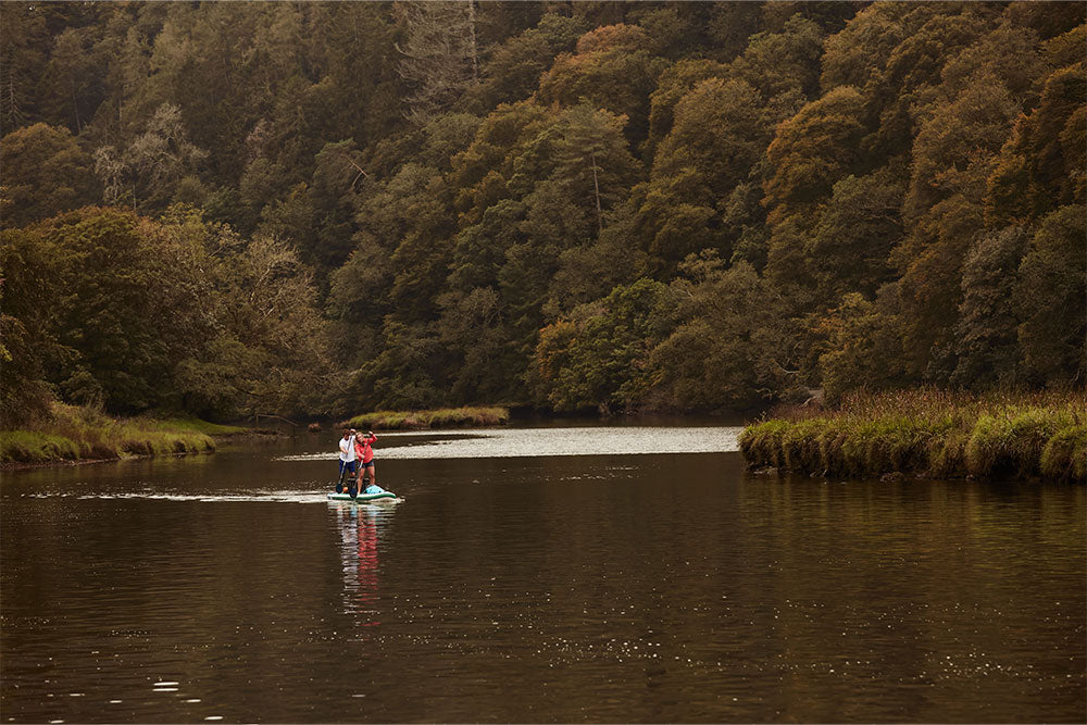 couple paddle boarding on a lake in the woods