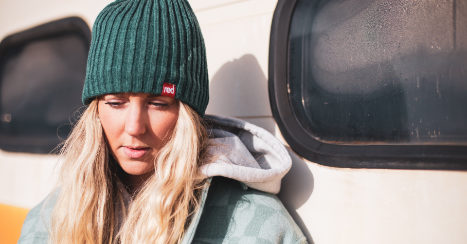 woman wearing teal knitted beanie standing by a campervan