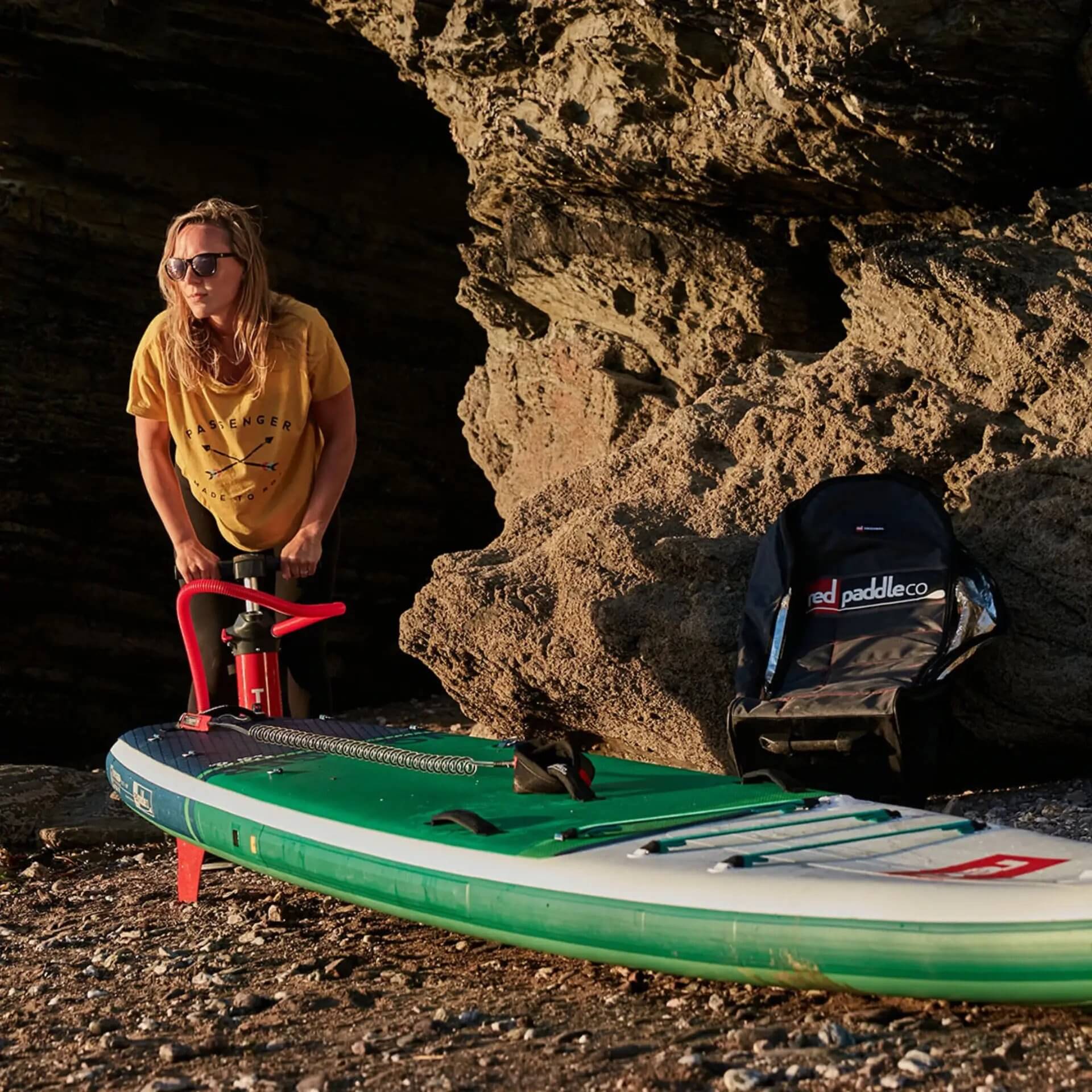 woman pumping up Red inflatable paddle board on a beach