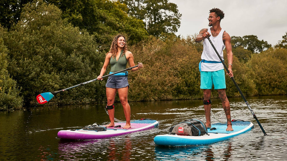 2 people paddle boarding alongside each other on Red inflatable paddle boards