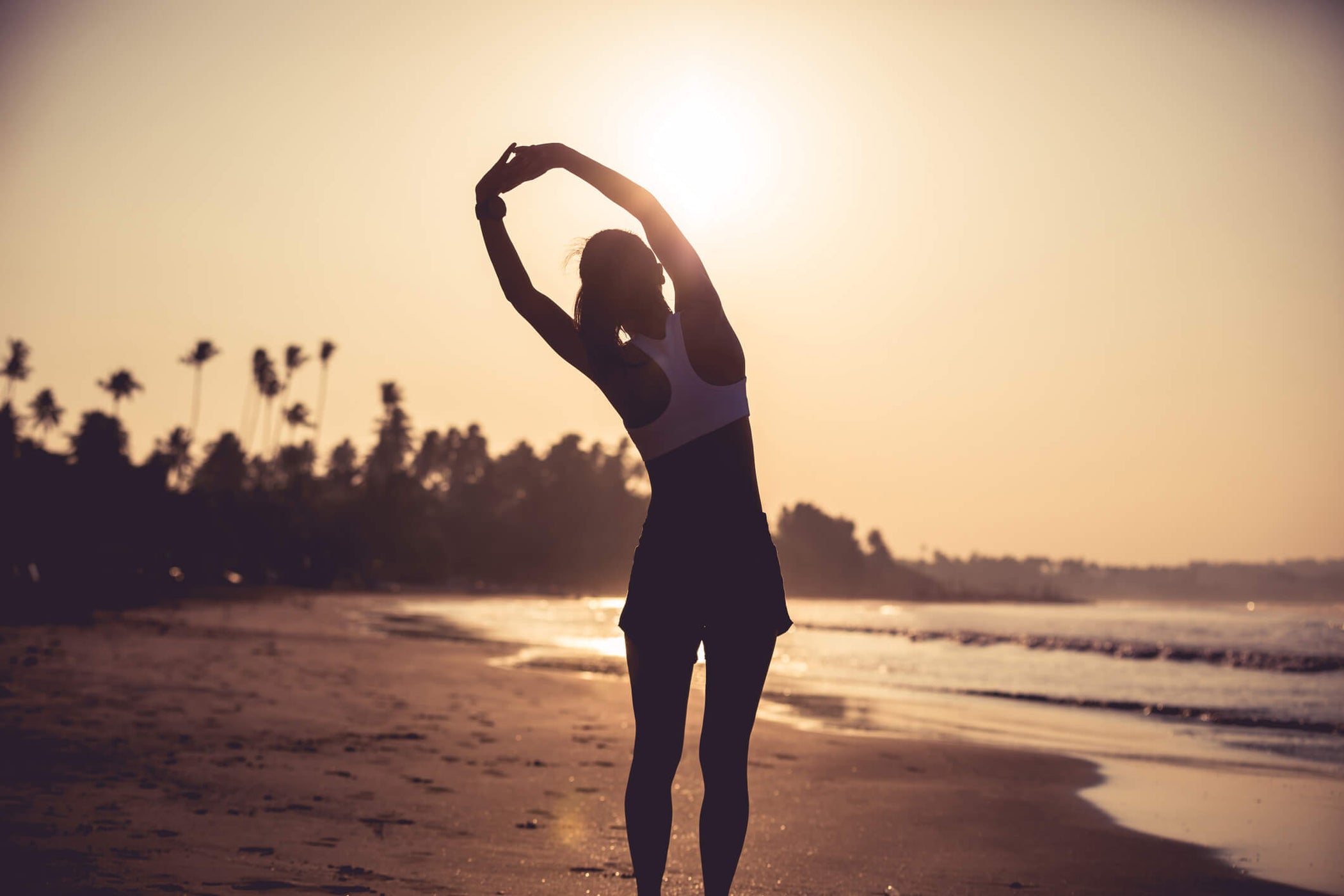 person doing a warm up exercise on a beach with the sun rising