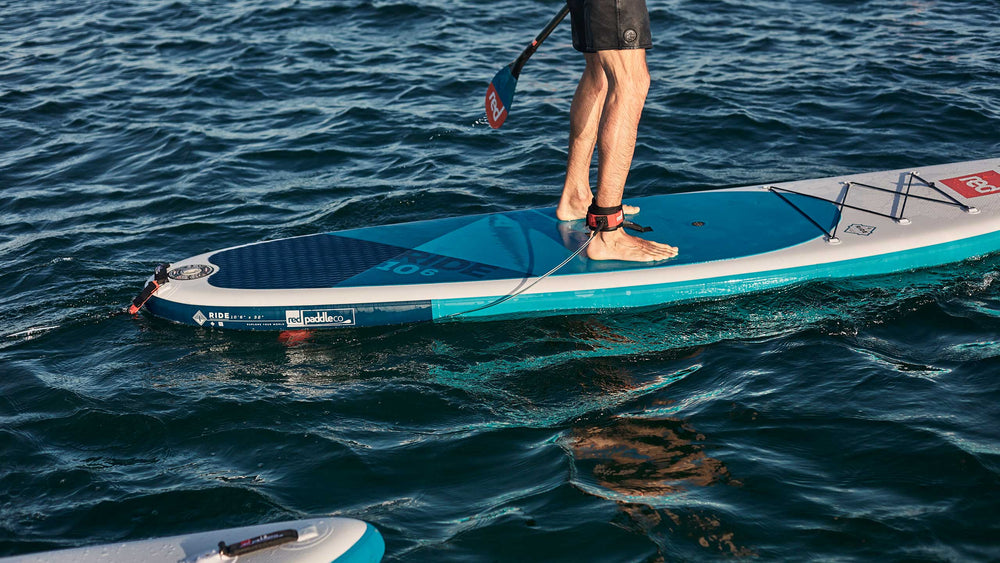 Man paddling on lake using Red Original straight SUP leash