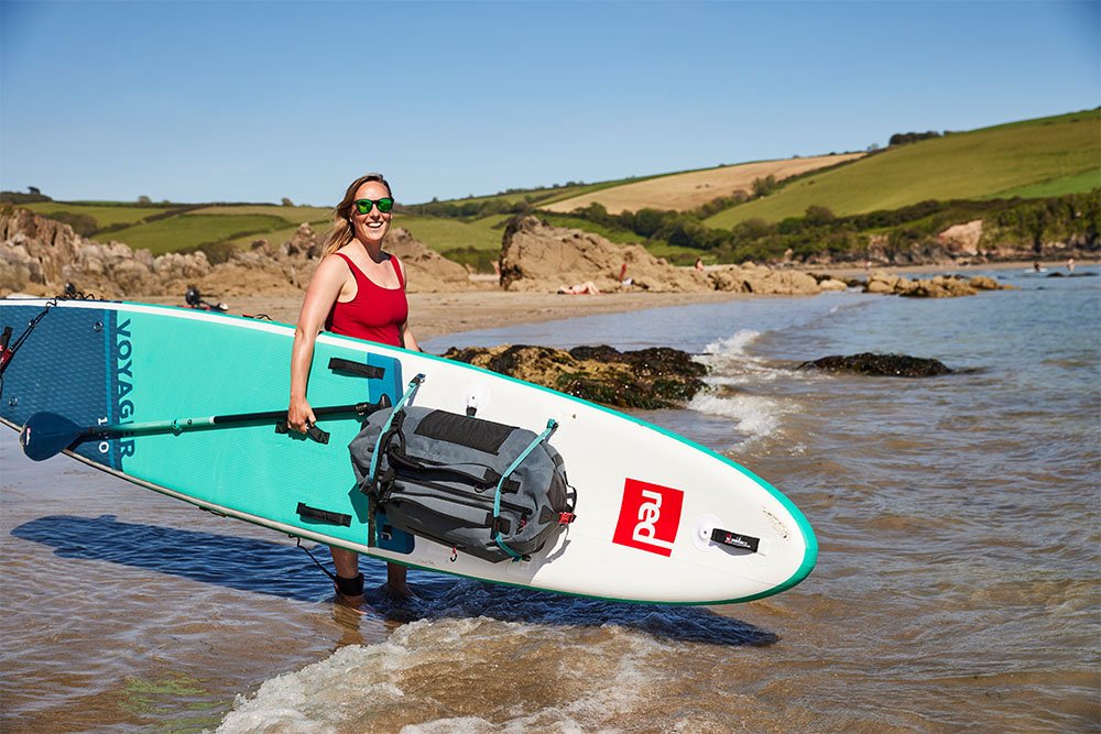 Woman carrying Red Original paddling board on beach