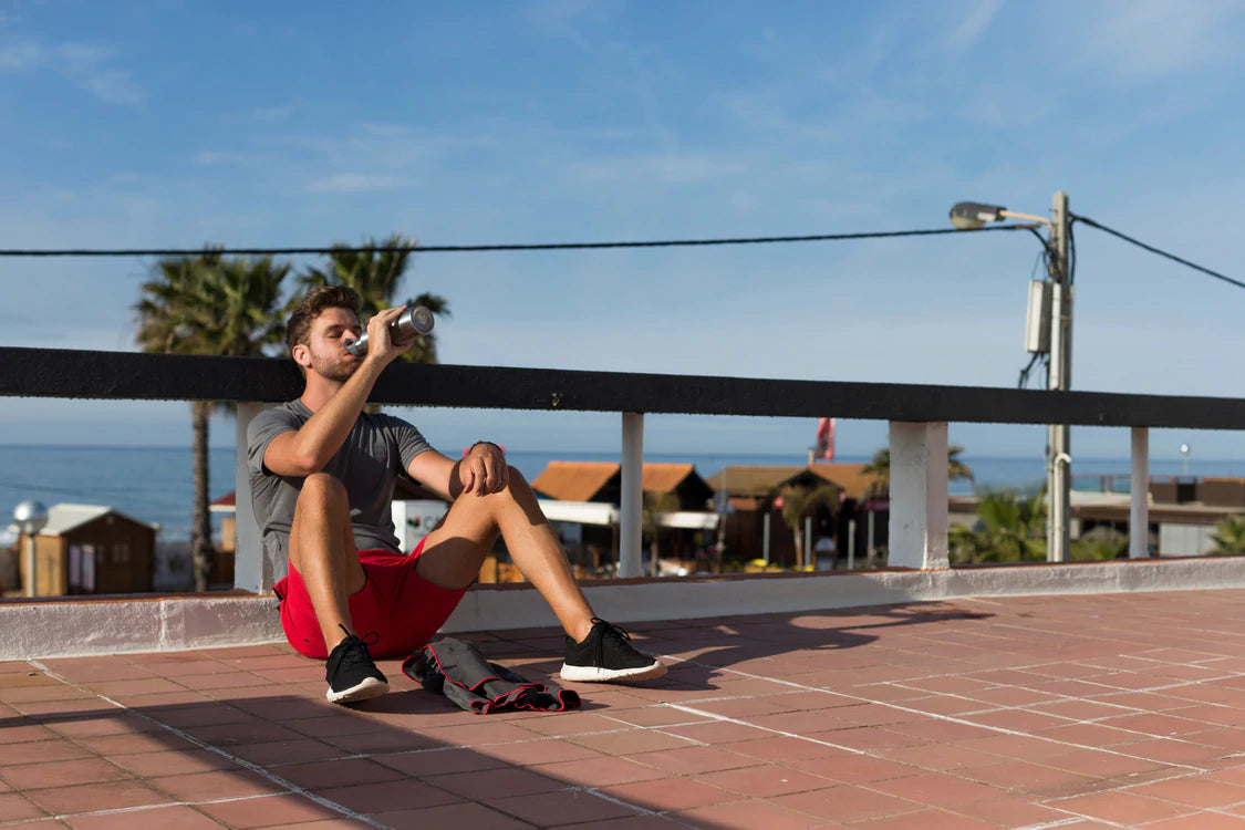 Man sat drinking from stainless steel water bottle near the beach