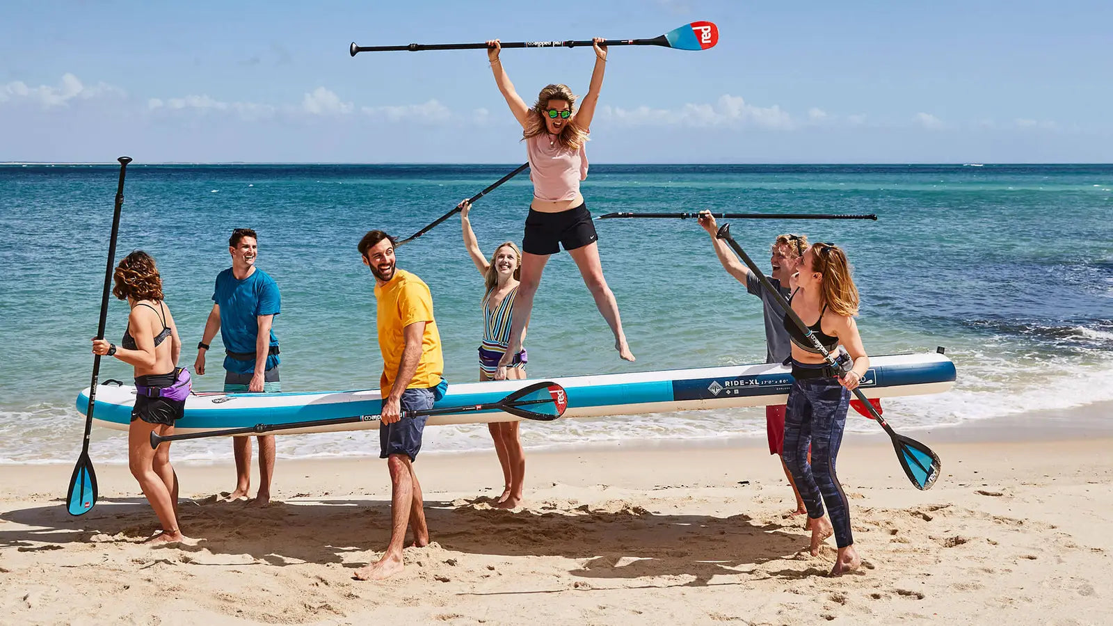 A group of people carrying a multi person paddleboard along the beach