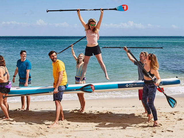 A group of people carrying a multi person paddleboard along the beach