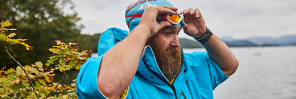 Bearded Man Wearing Wearing Hawaiian Blue Waterproof Changing Robe And Swim Cap Pulling Goggles Down