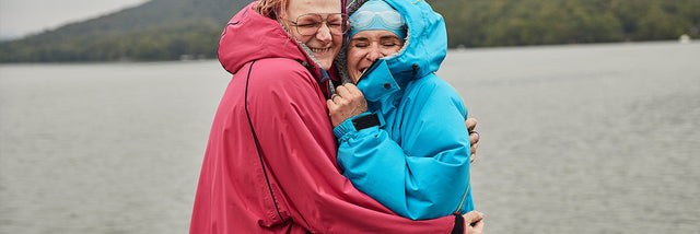 Two Women wearing Waterproof Changing Robes Hugging by a lake