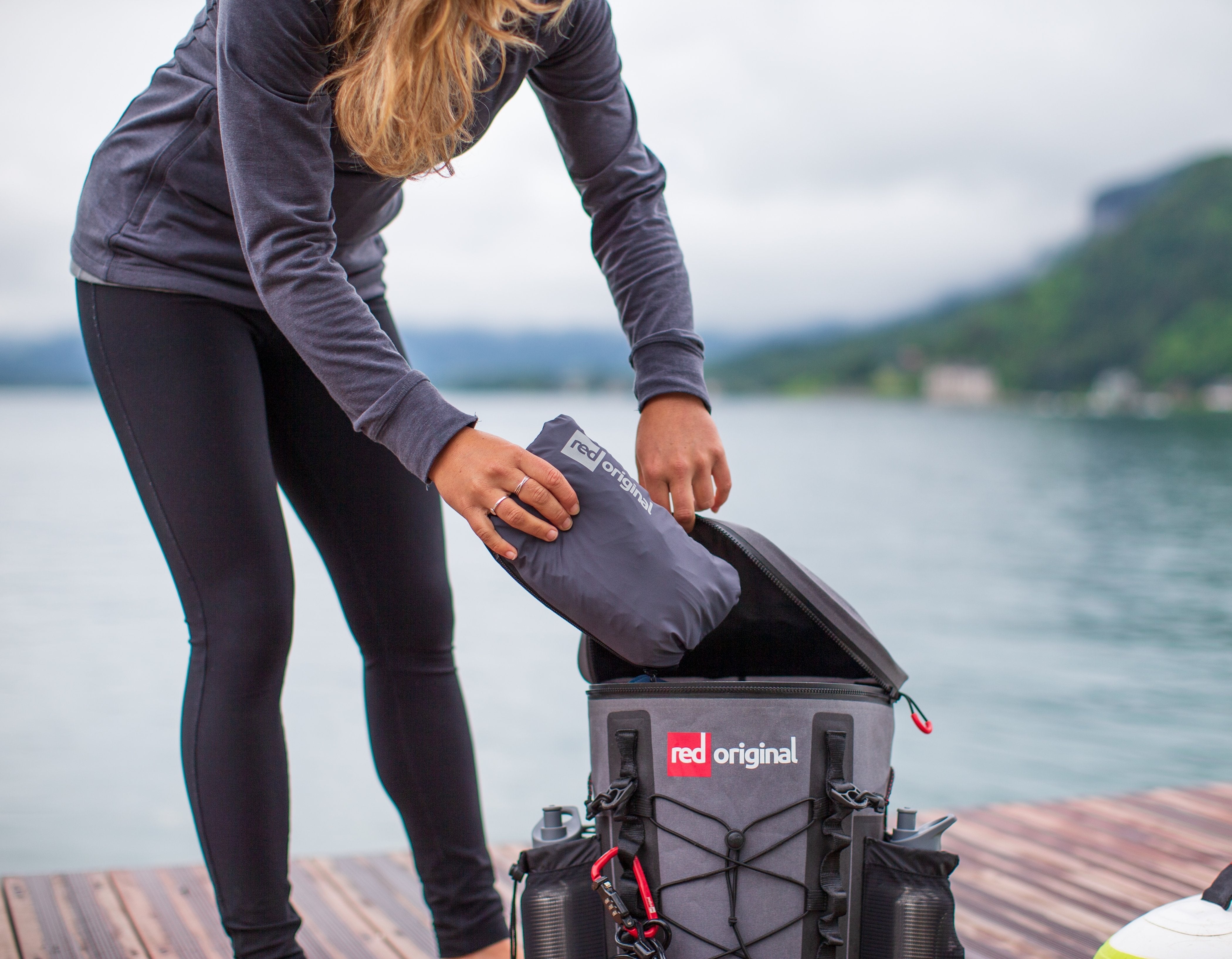 Woman placing active jacket into a deck bag beside a river. 