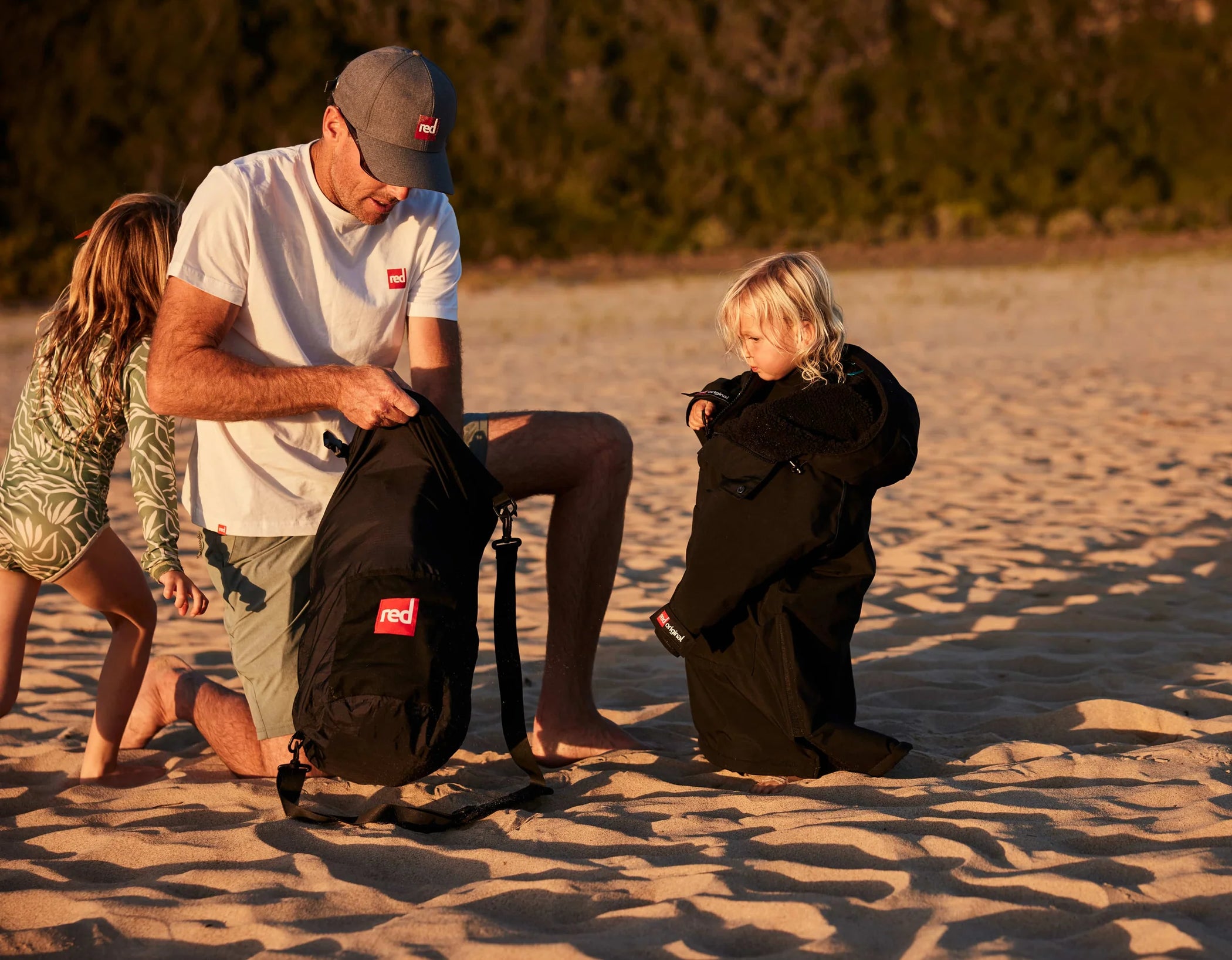 A man knelt on the beach packing stuff into his stash bag with his kids around him